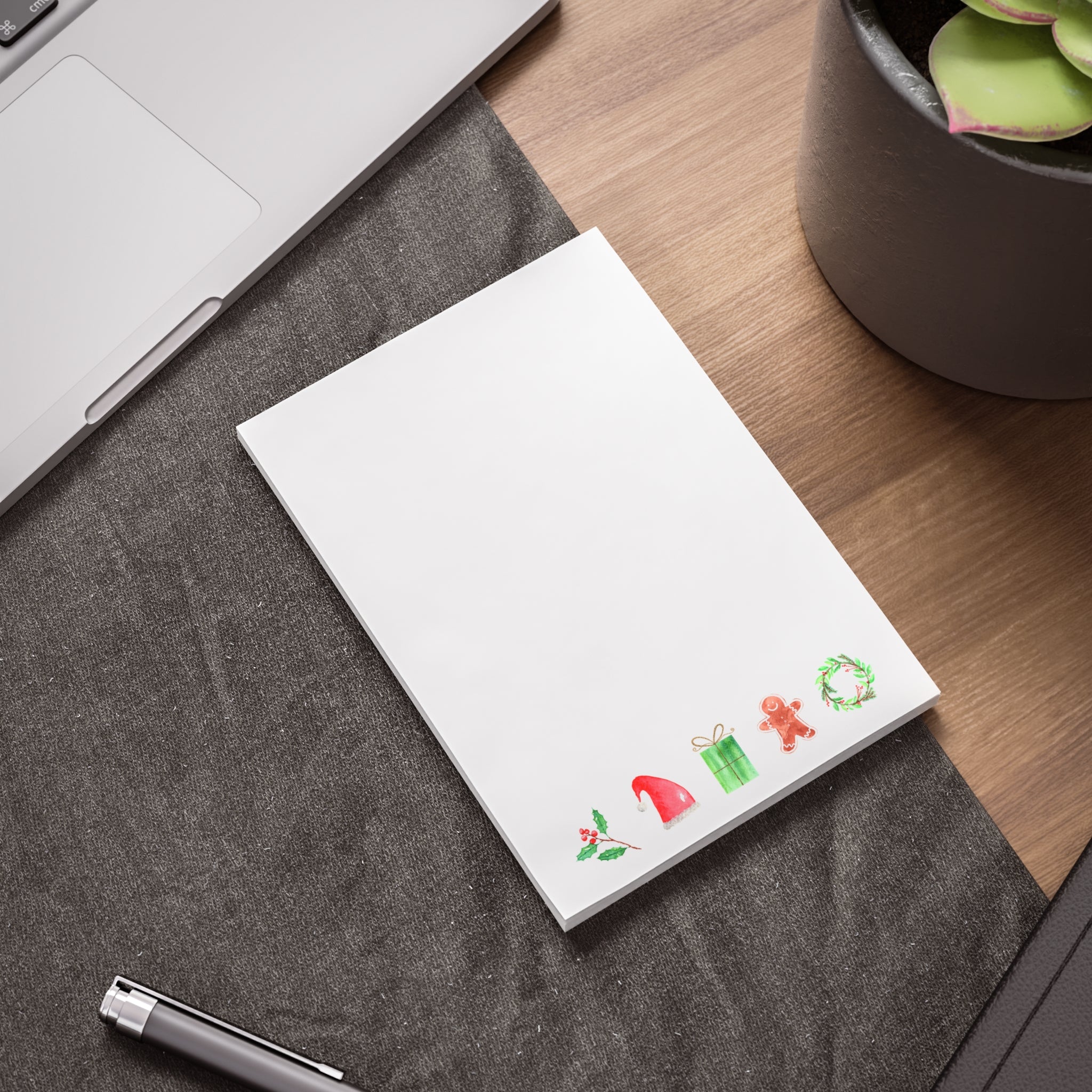 Notepad with Christmas-themed stickers on a desk with a laptop and plant.