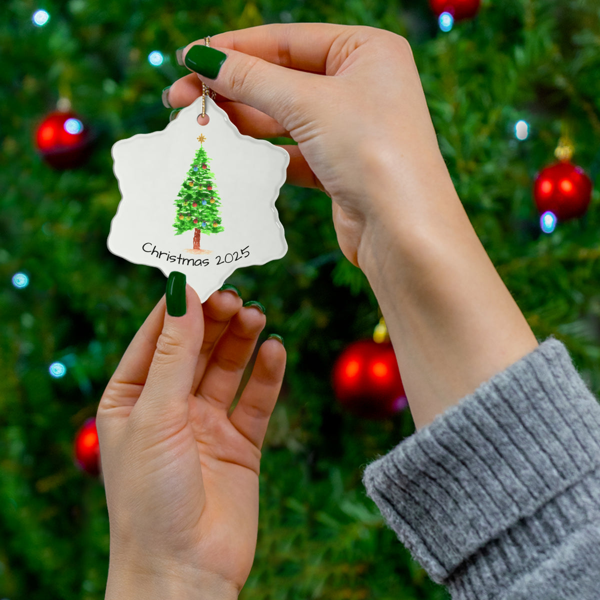 person holding a christmas ornament with a tree design and 'christmas 2025' text against a festive background.